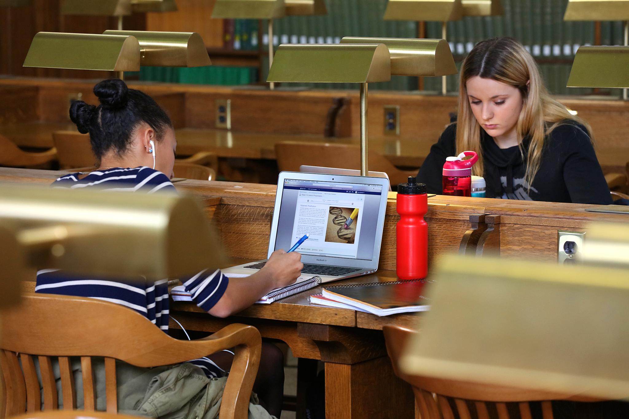 two students face each working at old fashioned wooden library tables