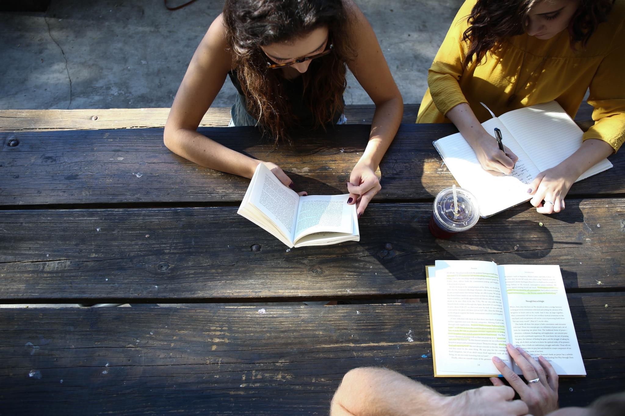 three students reading and writing on a picnic bench