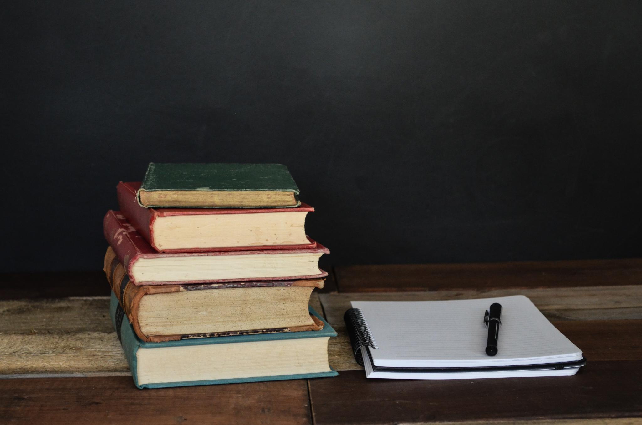on left a stack of books, on right a notepad, against a dark background